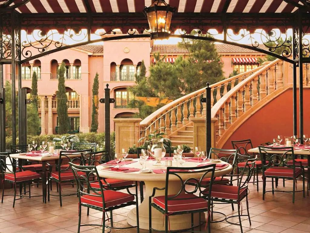 Outdoor tables beneath a striped awning beside a grand curved staircase