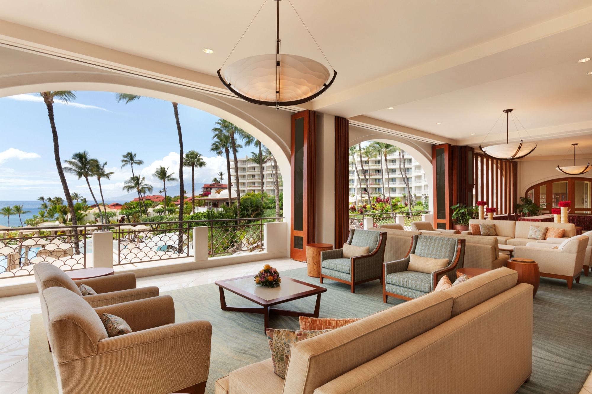 A lounge on the lobby mezzanine, open through tall arches to palms and the ocean