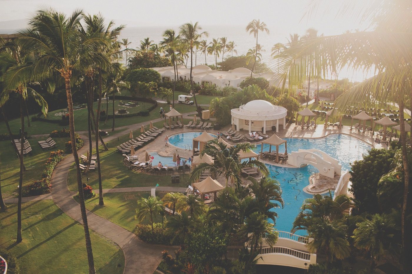 The resort's pools and white waterslide from above, with palms, cabanas, and the ocean beyond