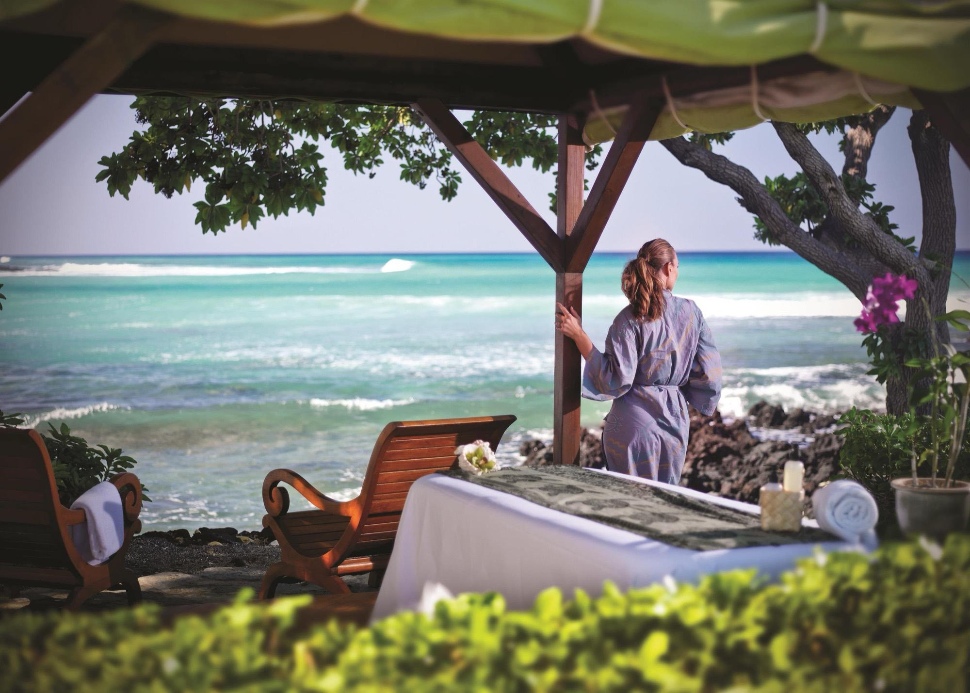 A guest in a robe at an open-air spa hut above the surf