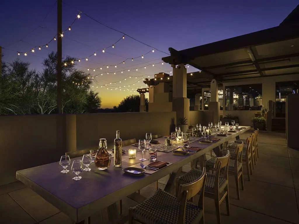 A long candlelit table on a terrace at dusk under string lights