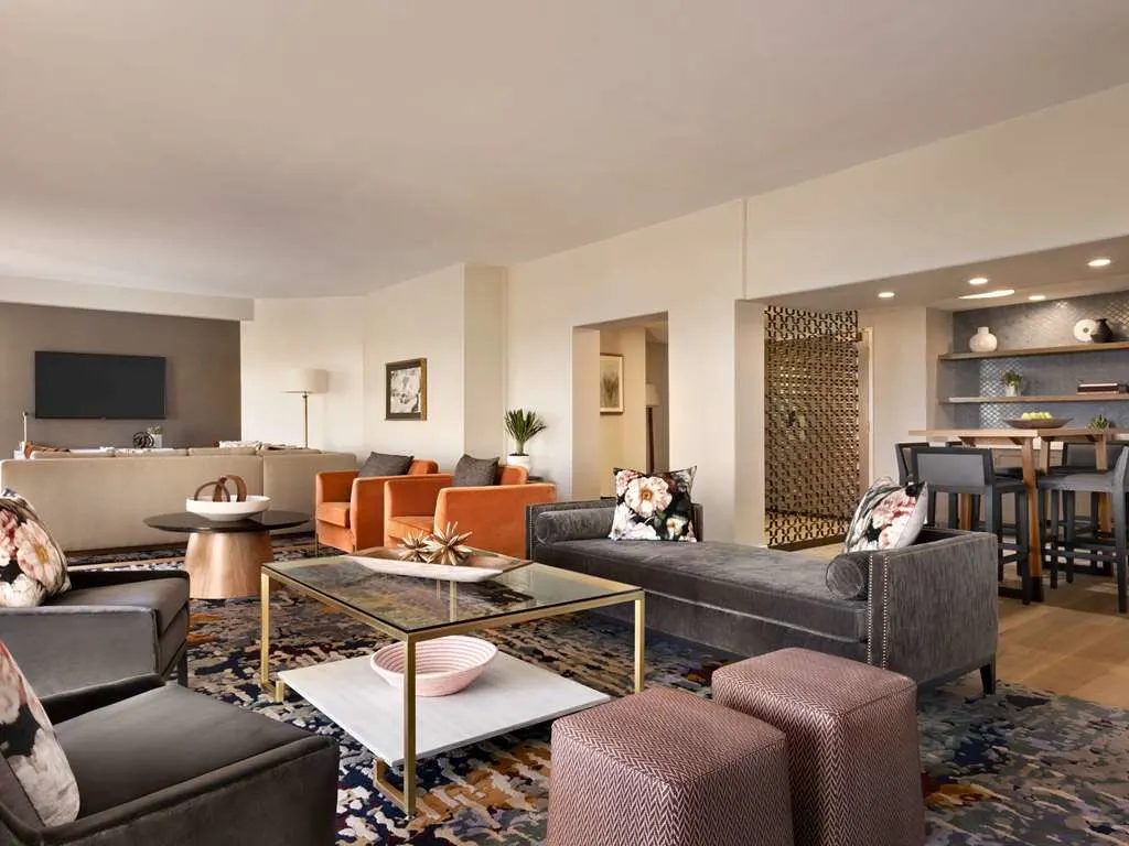 A suite living room with orange armchairs, gray sofas, and a dining area