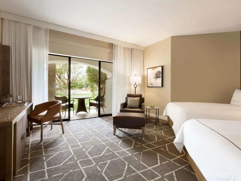 A room with two beds and doors open to a patio and green lawn