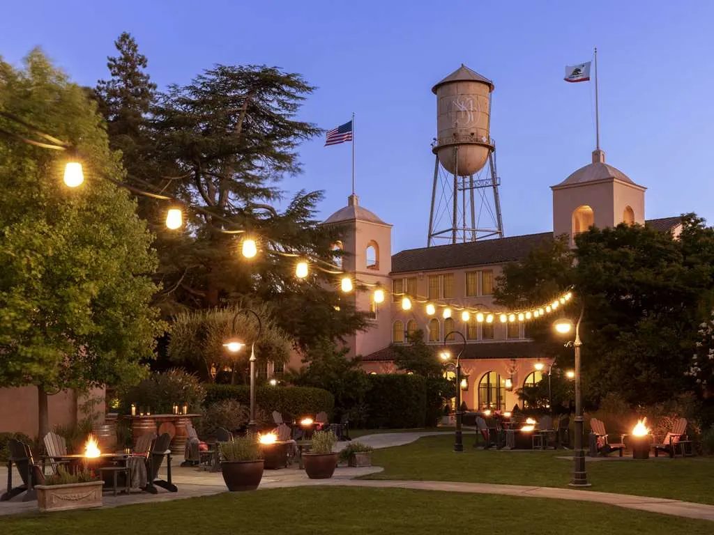 The lawn at dusk under string lights, with fire pits glowing and the old water tower beyond