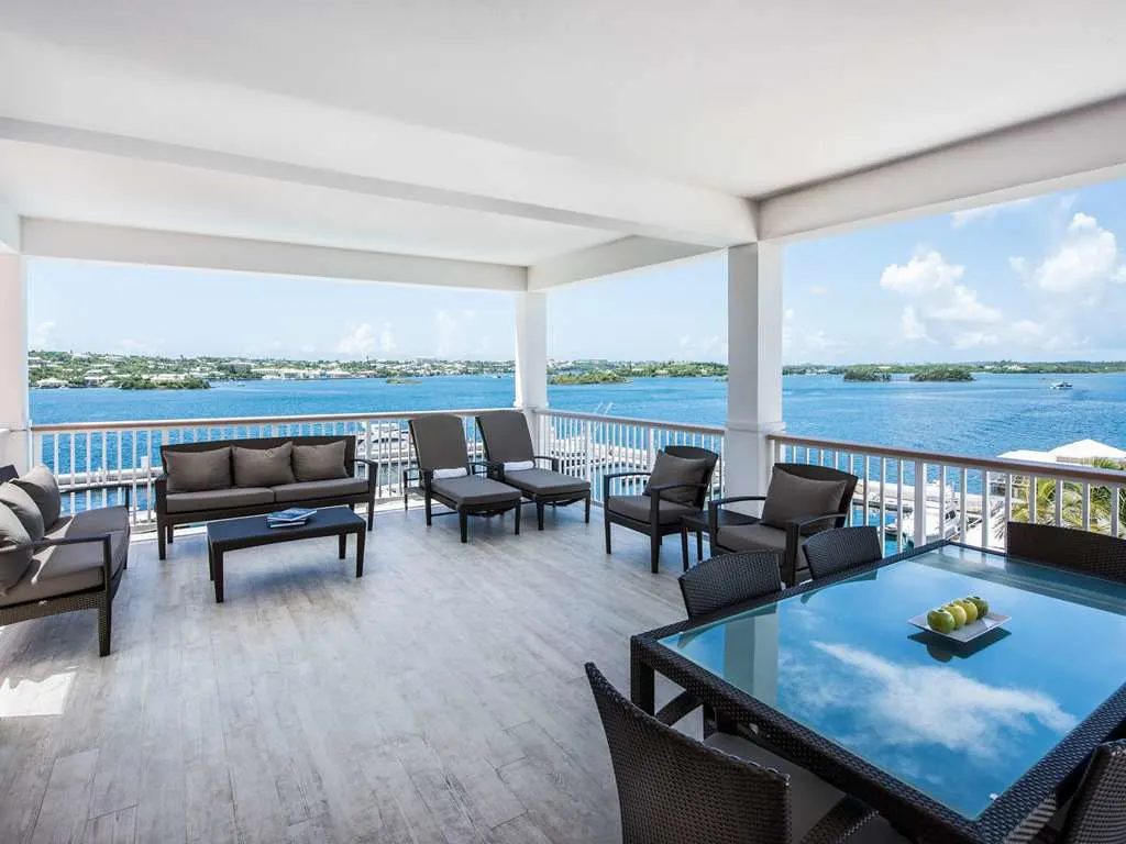 A covered lounge with sofas and a dining table above the harbor