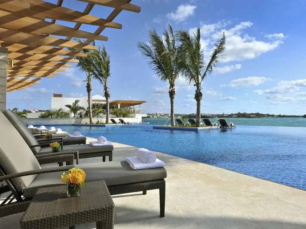 An infinity pool edged with loungers and palms, meeting the blue of Hamilton Harbour