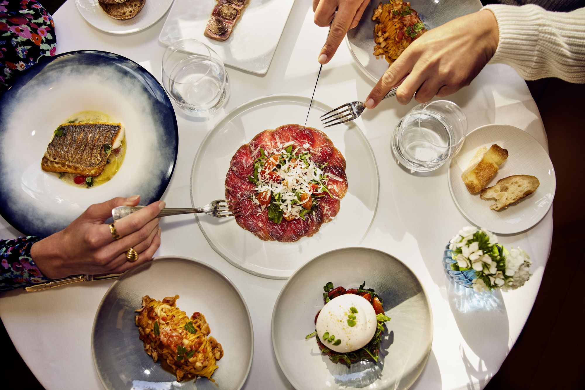 Plates of Italian dishes shared across a white table
