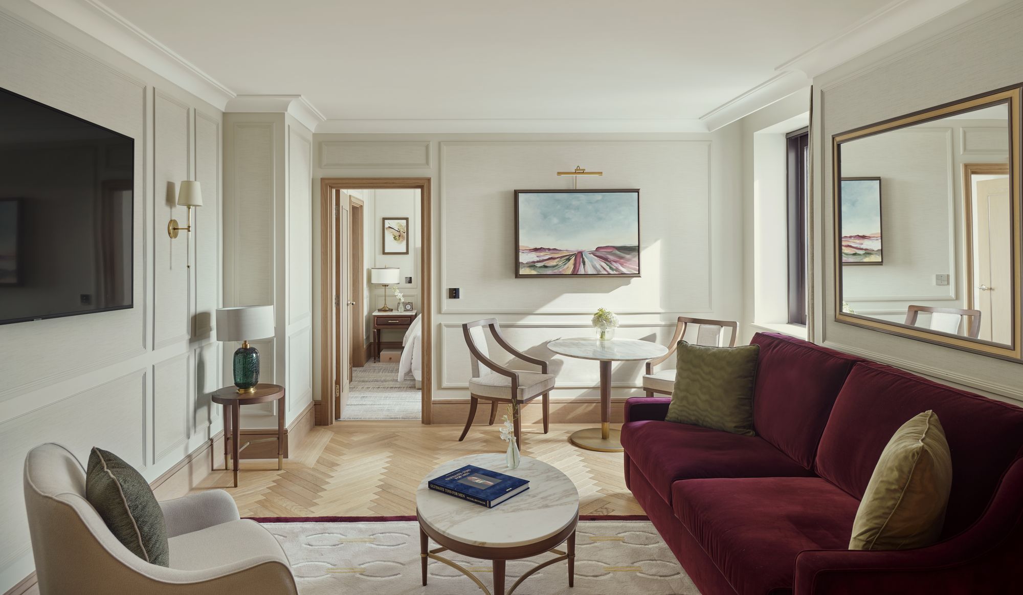 A suite living room with a plum sofa and a view through to the bedroom
