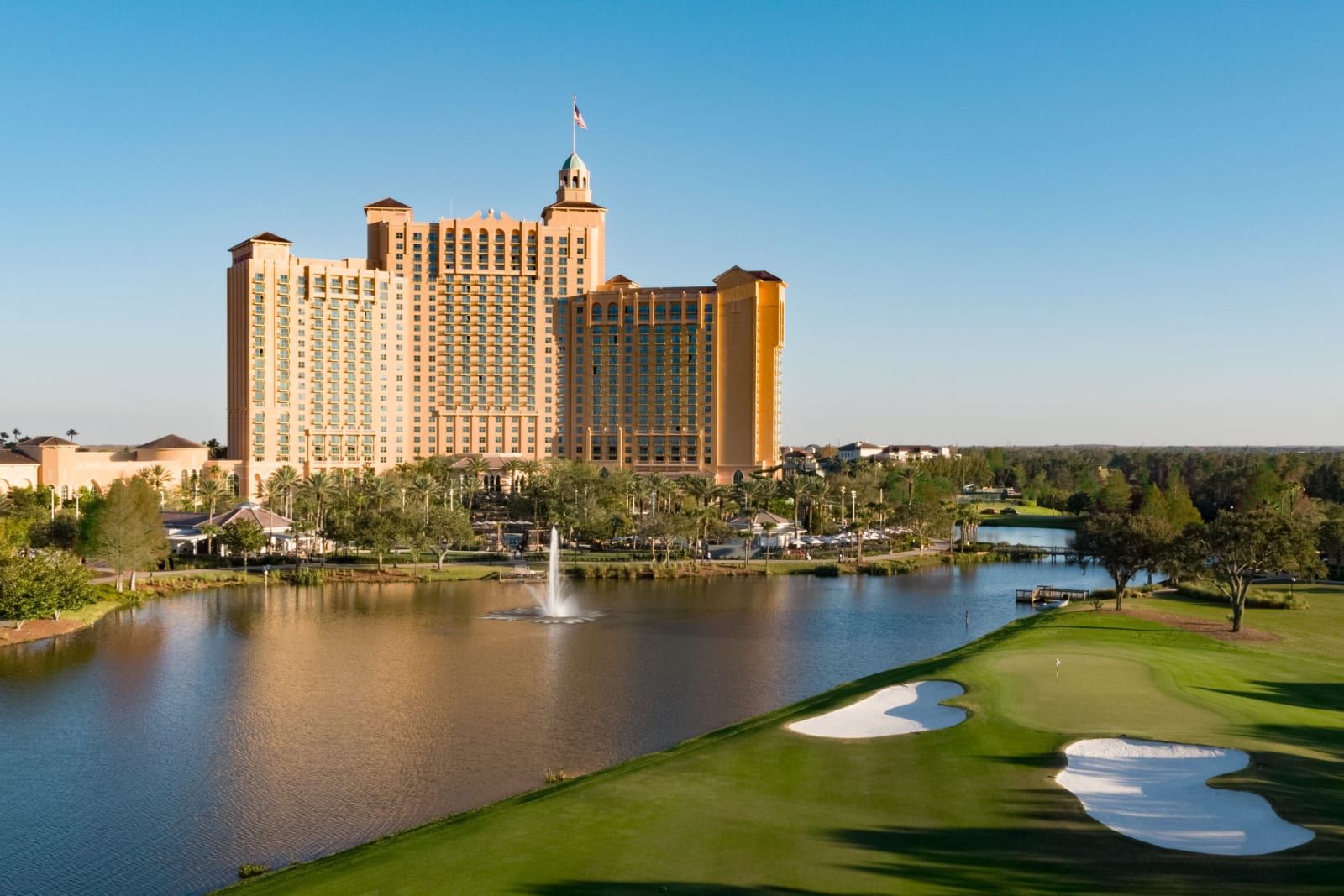 The resort tower across a lake and a green on the Greg Norman course