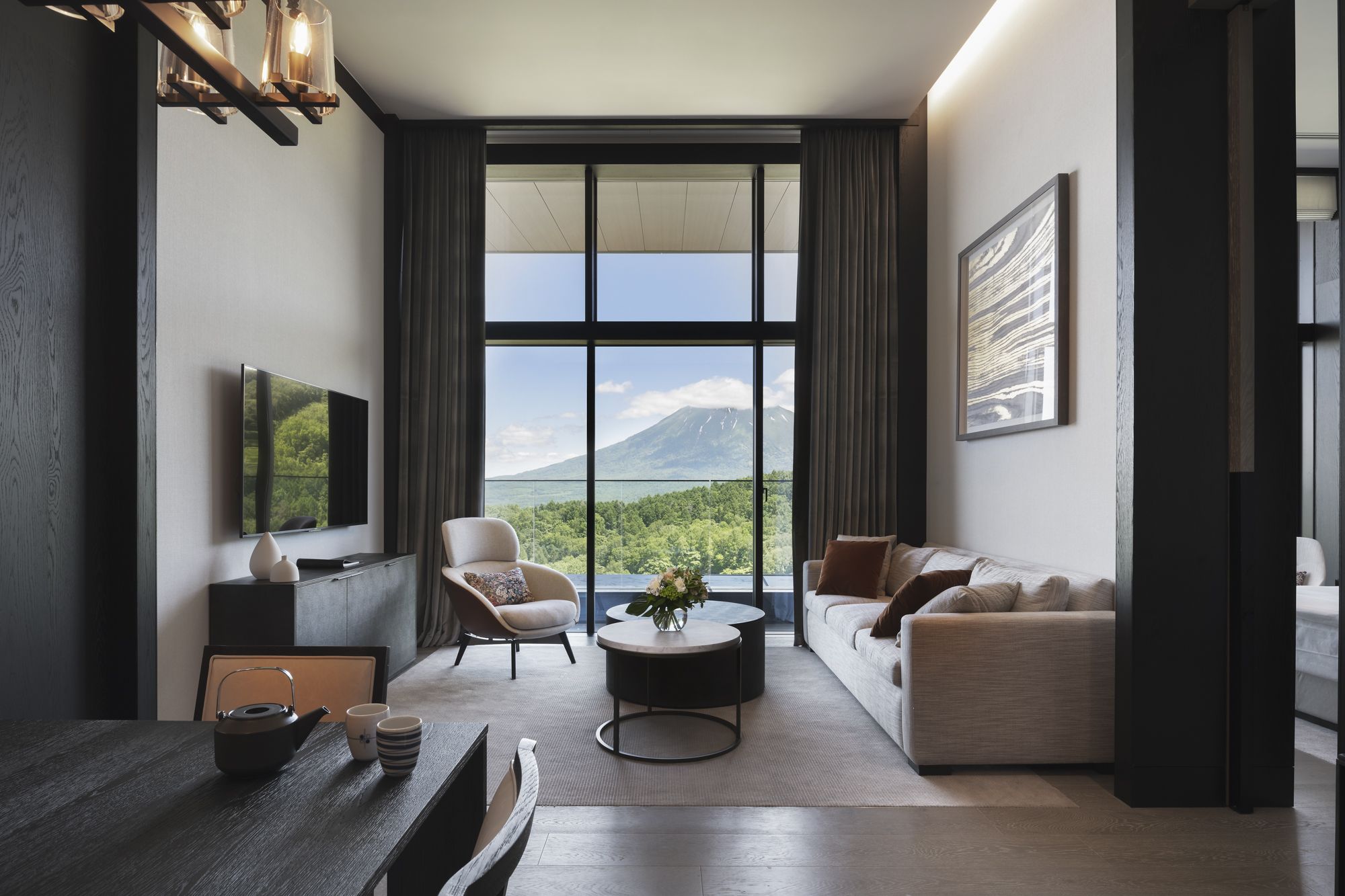 A penthouse living room with tall windows framing green hills and Mt. Yotei