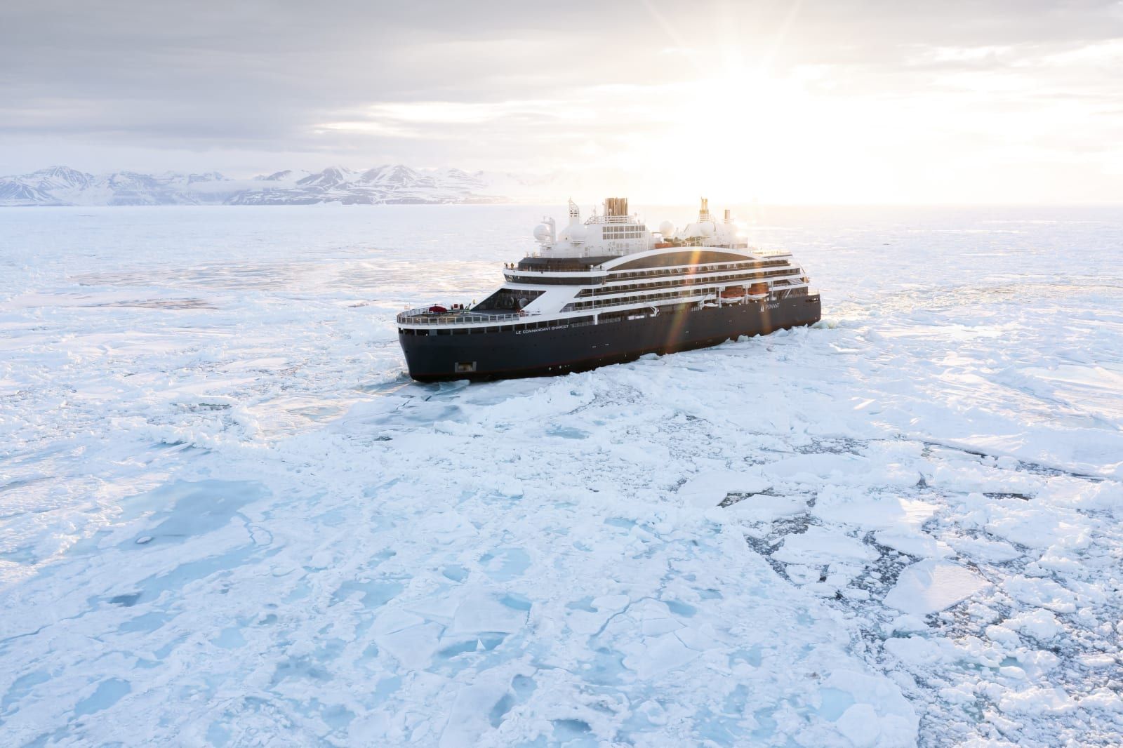 A PONANT icebreaker cutting through polar sea ice in low sun