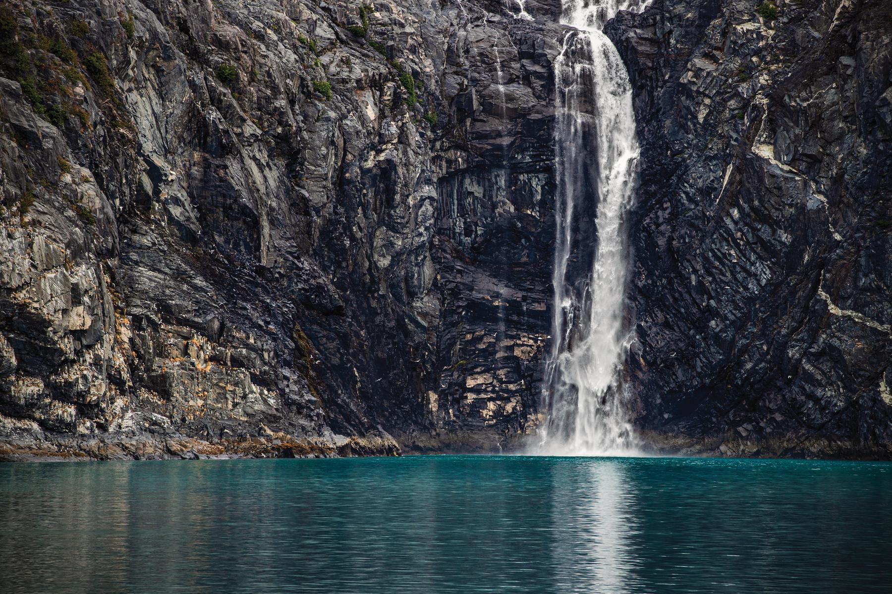 A waterfall pouring down dark cliffs into still turquoise water