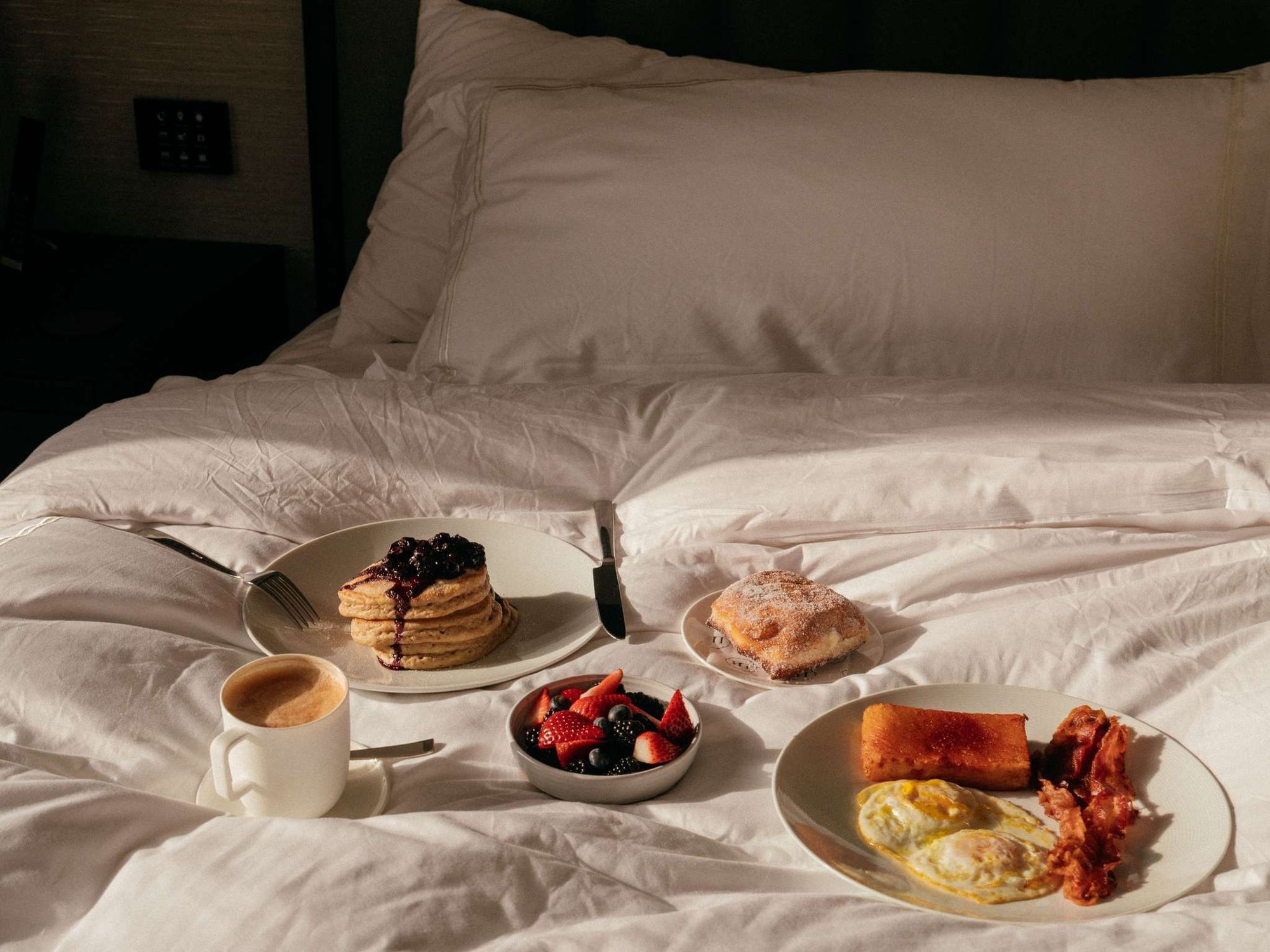 Breakfast in bed: pancakes, fruit, and coffee on white linens