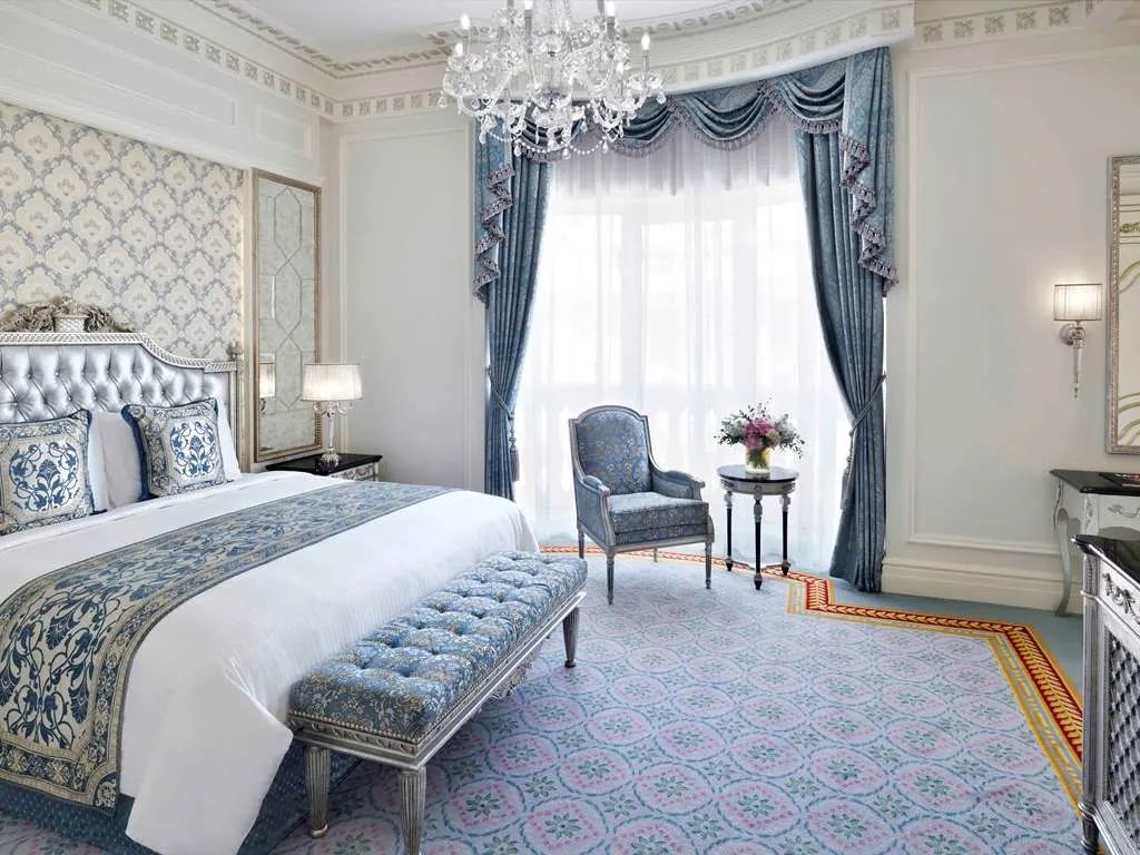 A bedroom in blue and white, with draped windows and a chandelier