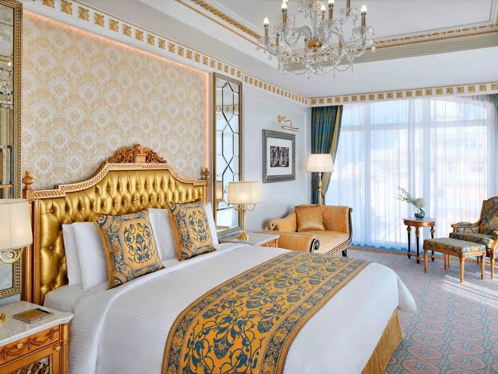 A bedroom with a gold tufted headboard beneath a crystal chandelier