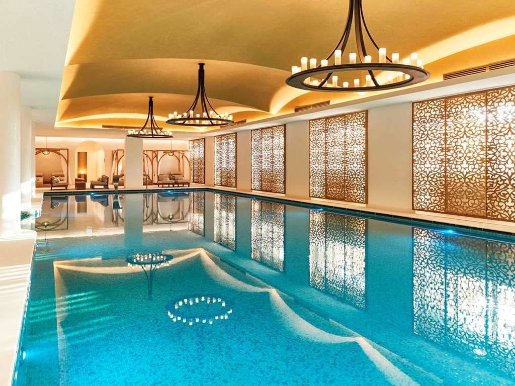 The long indoor pool beneath iron chandeliers and carved lattice screens