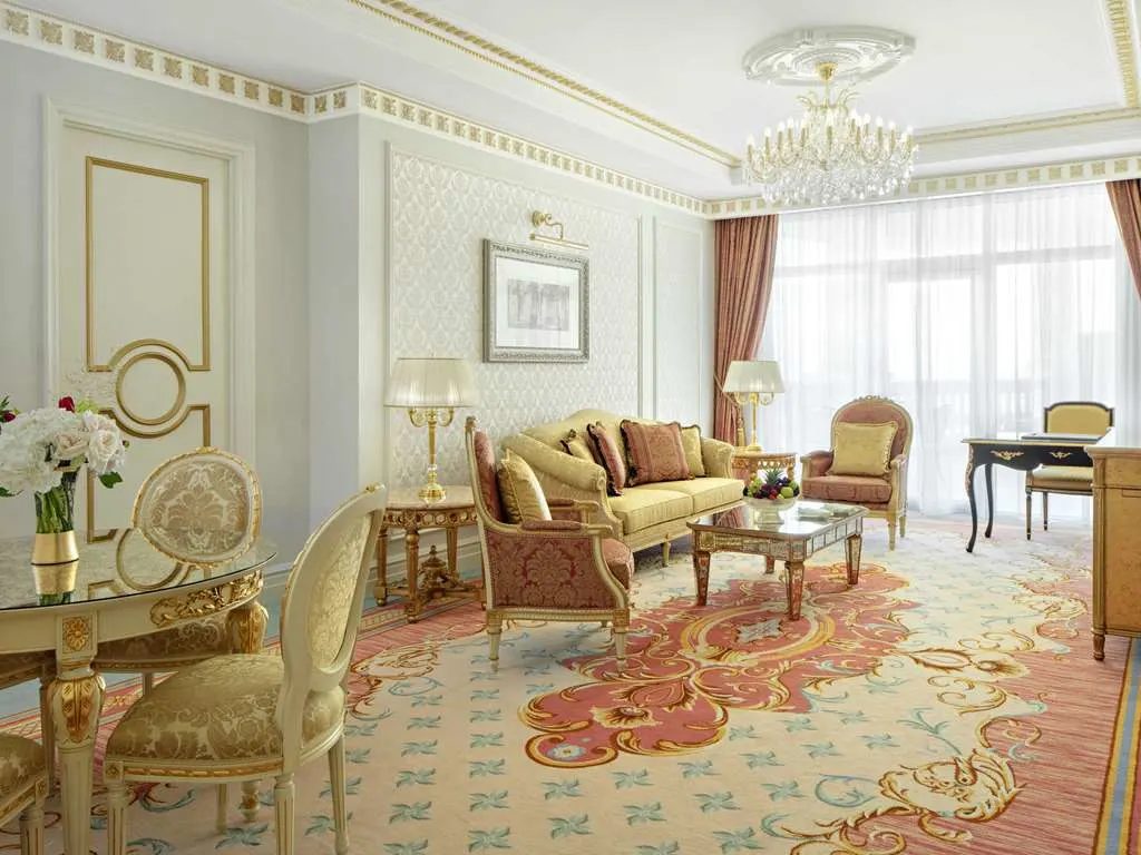 A suite living room with gilded furniture, a crystal chandelier, and a patterned carpet