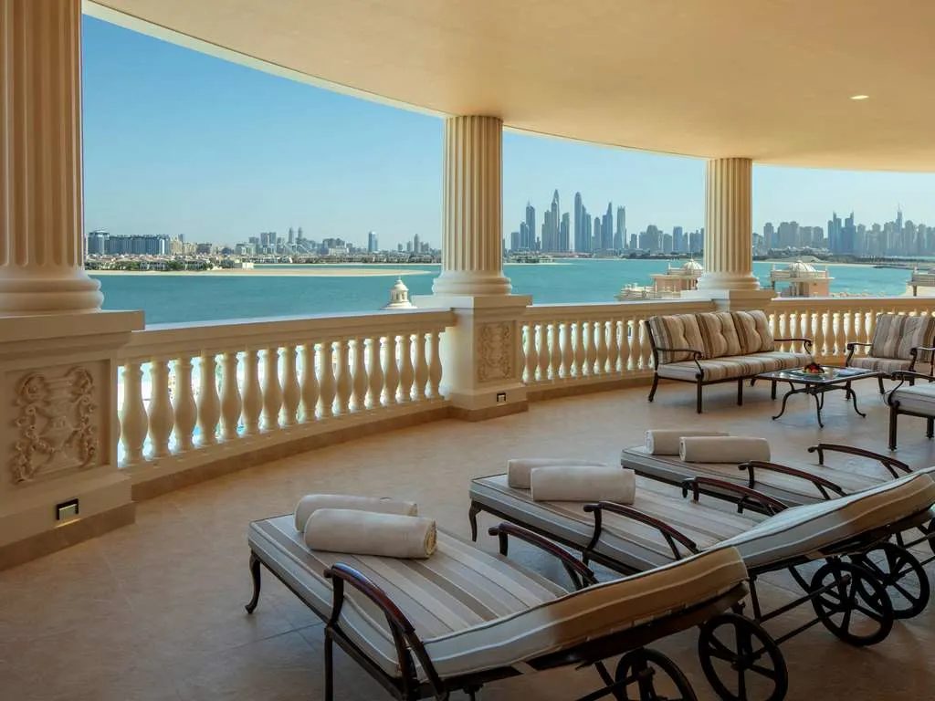 A colonnaded terrace with loungers, looking across the sea to the Dubai Marina skyline