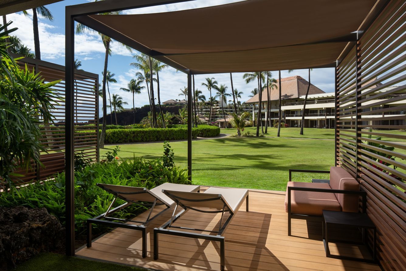 A shaded garden lanai with loungers facing the lawn