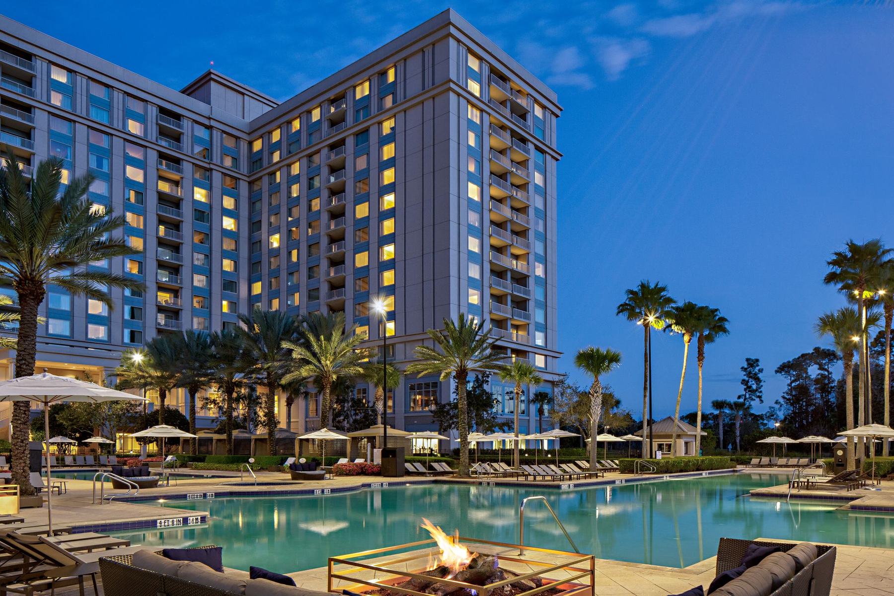 The resort pool at dusk, with fire pits and palms in front of the Waldorf Astoria Orlando tower